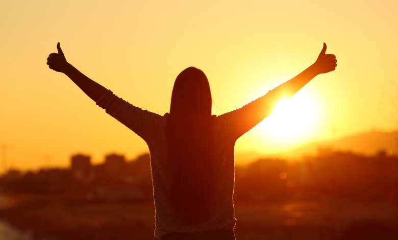 Backlight of a woman raising arms with thumbs up