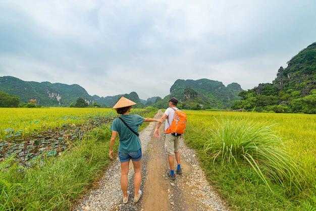 couple-walking-hand-hand-road-among-rice-fields-man-with-backpack-woman-with-vietnamese-hat-having-fun-ninh-binh-vietnam