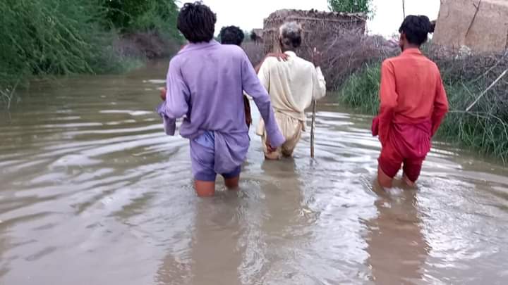Villagers wading through floodwater in a village of Sindh
