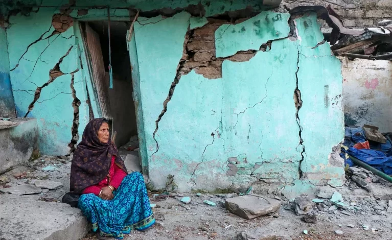 A woman sits beside a cracked wall of her house at Joshimath in Chamoli district of India's Uttarakhand state