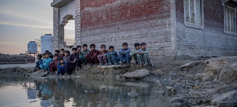 Children sit beside a pond of contaminated flood water in Sindh province