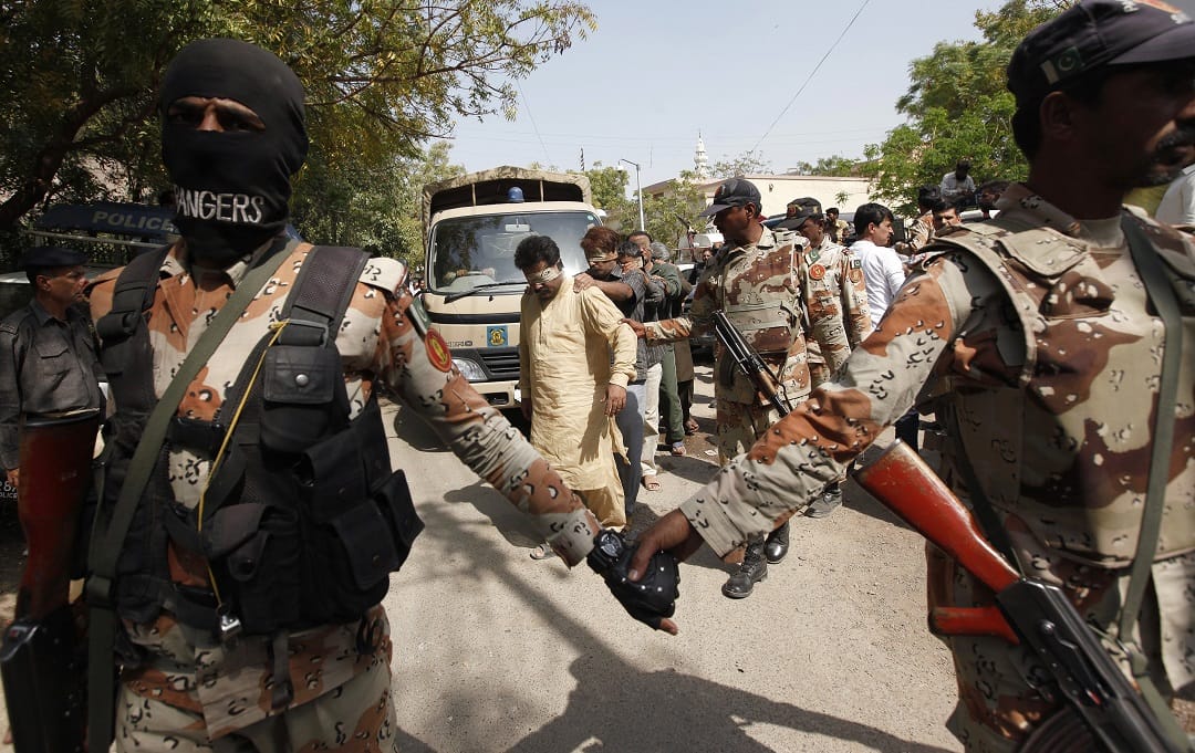 Paramilitary soldiers hold hands as fellow soldiers escort blindfolded men detained during the raid at the MQM headquarters ahead of their court appearance in Karachi
