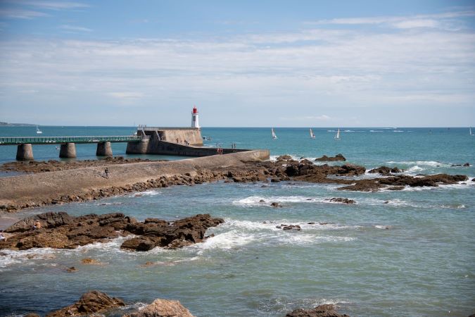free-photo-of-rocks-on-sea-shore-with-lighthouse-behind