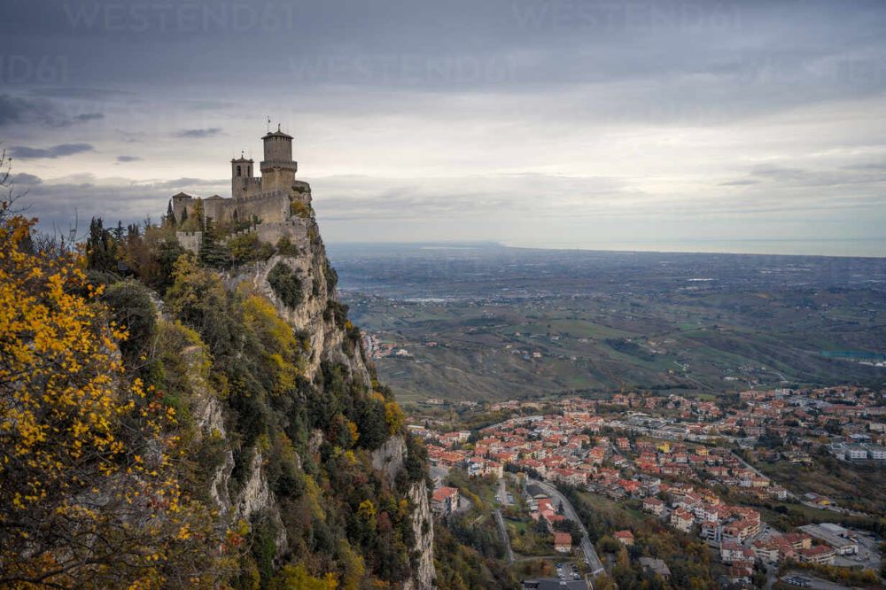 ancient-castle-on-peak-overgrown-with-green-trees-raising-high-into-gray-sky-in-san-marino-italy-ADSF12565